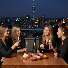 Load image into Gallery viewer, Four women enjoying a meal with a bottle of Cable Bay Cinders Vineyard Sauvignon Blanc white wine and charcuterie board on a rooftop at night.