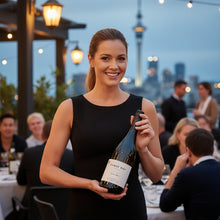Load image into Gallery viewer, Woman holding a bottle of Cable Bay Reserve Pinot Gris wine at an outdoor event with city skyline in the background
