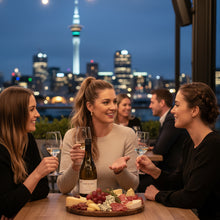 Load image into Gallery viewer, Three women enjoying a meal with a bottle of Cable Bay Reserve Pinot Gris wine and cheese platter against a city skyline at night.