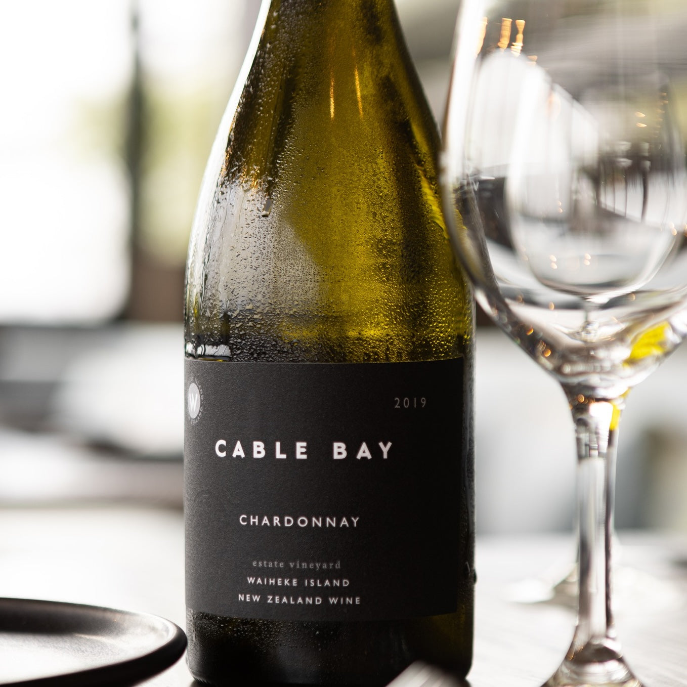 Load image into Gallery viewer, A bottle of Cable Bay Waiheke Island Chardonnay on a table with a wine glass