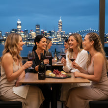 Load image into Gallery viewer, Group of women enjoying a bottle of Cable Bay Waiheke Island Syrah wine and food at a table with a city skyline in the background