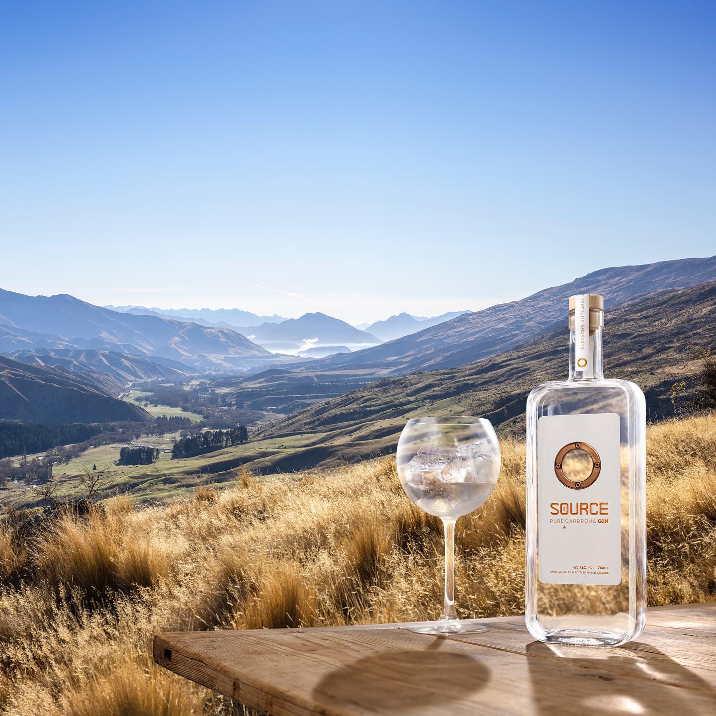 Load image into Gallery viewer, Bottle and glass of 'Source' on a wooden table with a scenic mountain view.