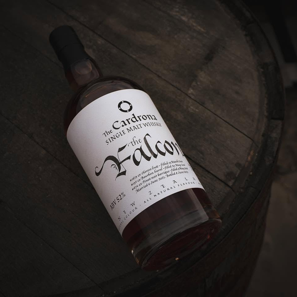 Load image into Gallery viewer, A bottle of The Cardrona 'The Falcon' Single Malt Whisky resting diagonally on a dark wooden barrel.