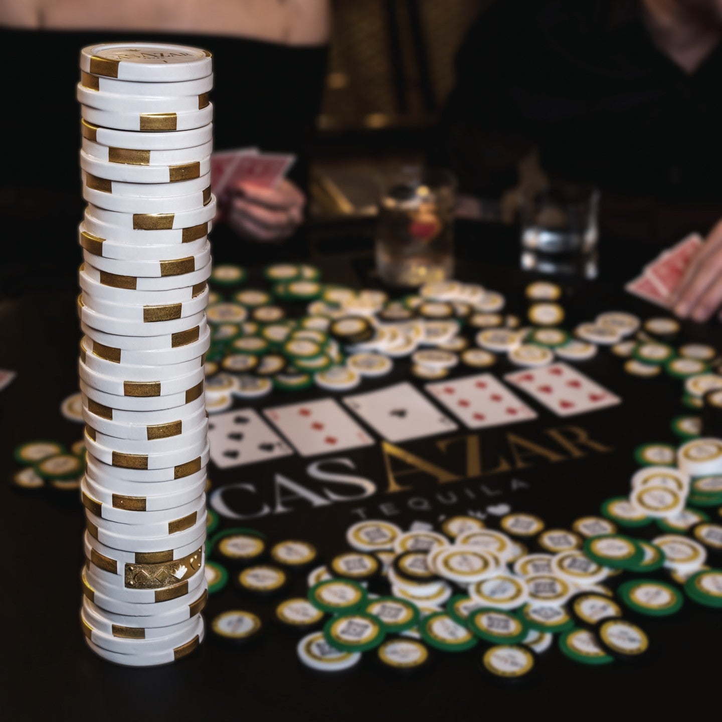 Load image into Gallery viewer, Scattered poker chips on a casino-themed table with playing cards and a bottle of CasAzar Joven Tequila on the table
