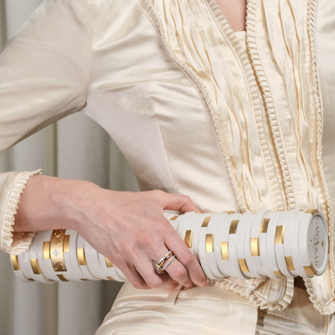 Load image into Gallery viewer, A woman wearing a coloured outfit with gold accents, holding a bottle of CasAzar Joven Tequila.