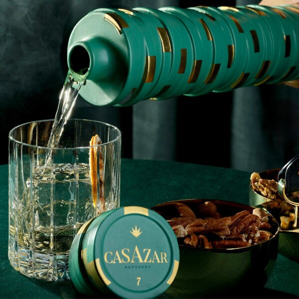 Load image into Gallery viewer, CasAzar Reposado Tequila bottle being poured into a glass with decorative elements on a dark background.