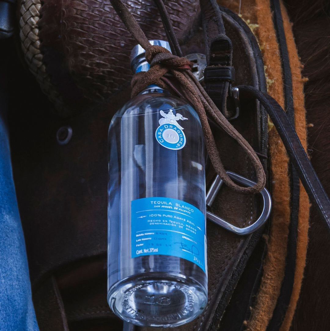 Load image into Gallery viewer, Casa Dragones Blanco Tequila bottle with blue label on a leather surface
