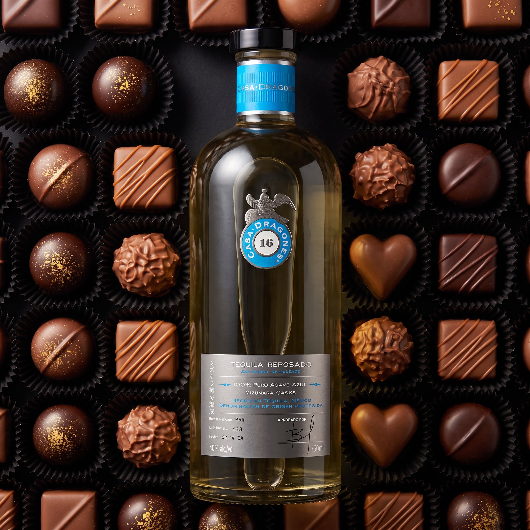 Load image into Gallery viewer, A bottle of Casa Dragones Reposado Mizunara Tequila centred against a background of assorted chocolate truffles and squares. The bottle has a black cap, a blue neck label, and a grey label with a circular blue and white logo.