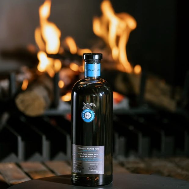 Load image into Gallery viewer, A bottle of Casa Dragones Reposado Mizunara Tequila set on a dark surface with a blurred fireplace in the background.