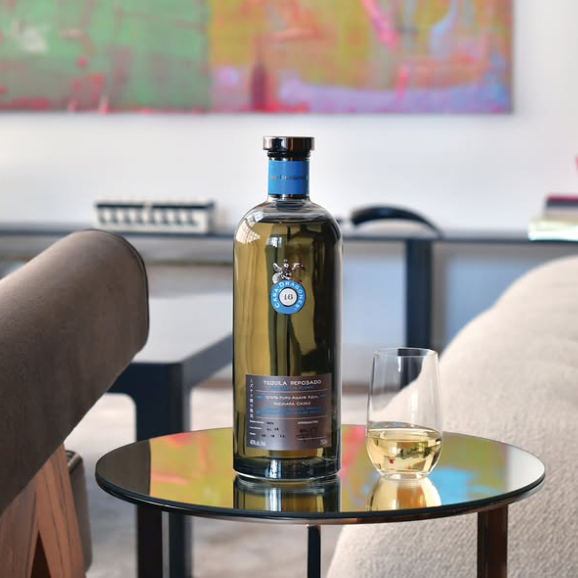 Load image into Gallery viewer, A bottle of Casa Dragones Reposado Mizunara Tequila sits on a small round table next to a filled whisky glass in a modern living room setting.