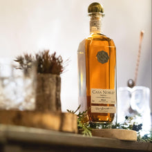 Load image into Gallery viewer, Casa Noble Anejo tequila bottle on a decorative surface with blurred background