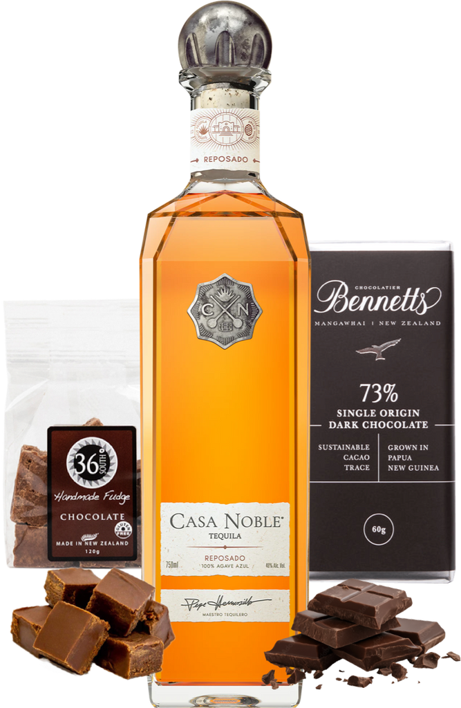 A bottle of Casa Noble Reposado Tequila centered on a white background, flanked by a bag of 36 Degrees Handmade Chocolate Fudge and a bar of Bennett's 73% Single Origin Dark Chocolate, with chocolate pieces scattered at the base