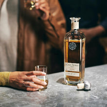 Load image into Gallery viewer, Casa Noble reposado tequila bottle with a glass on a table, blurred people in the background