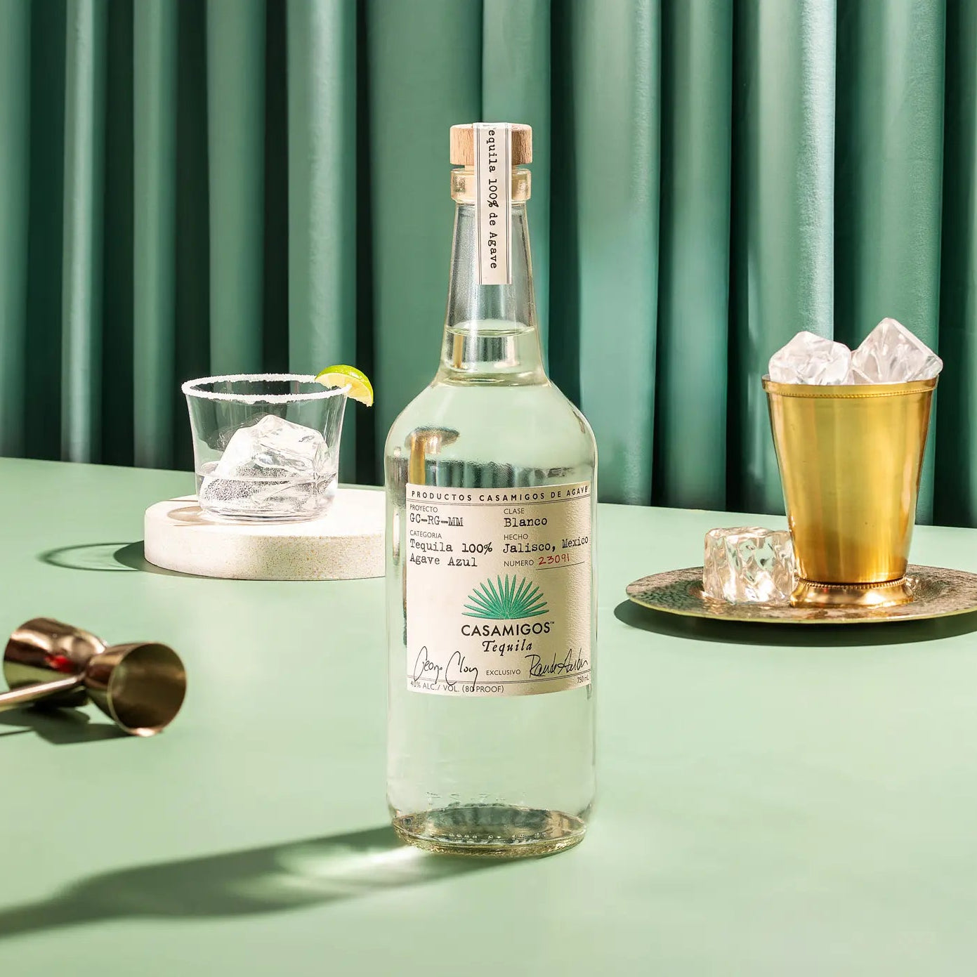 Load image into Gallery viewer, Casamigos blanco tequila bottle on a green table with glasses and lime garnish.