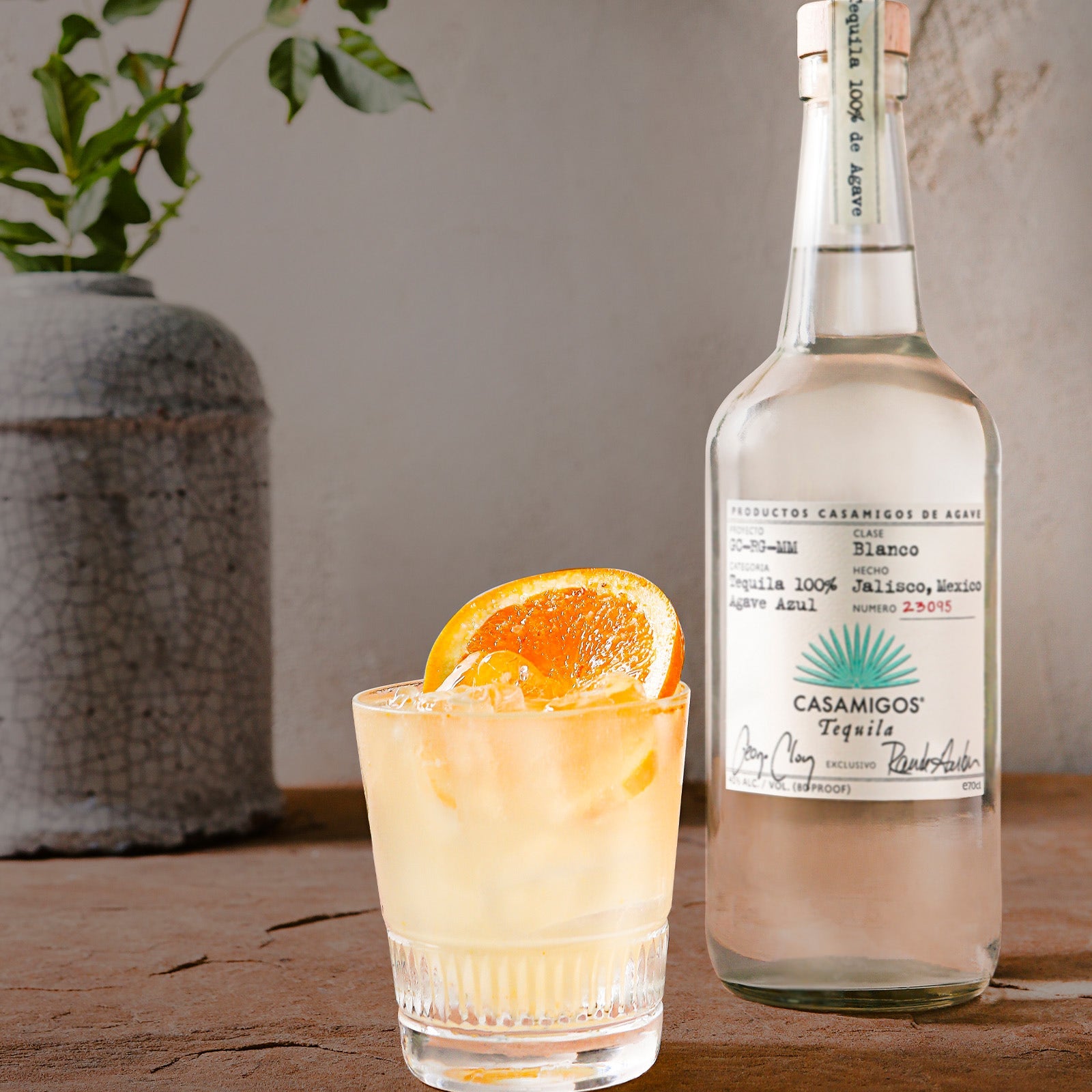 Load image into Gallery viewer, Cocktail with orange slice and bottle of Casamigos blanco tequila on wooden surface.