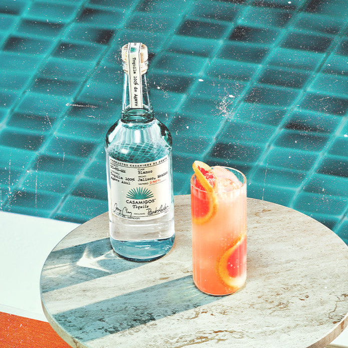 Load image into Gallery viewer, Cocktail and Casamigos Blanco Tequila bottle on a table with pool background and 'House of Friends' text.