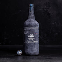 Load image into Gallery viewer, Dark black bottle with &#39;Casamigos Mezcal&#39; label on a black background
