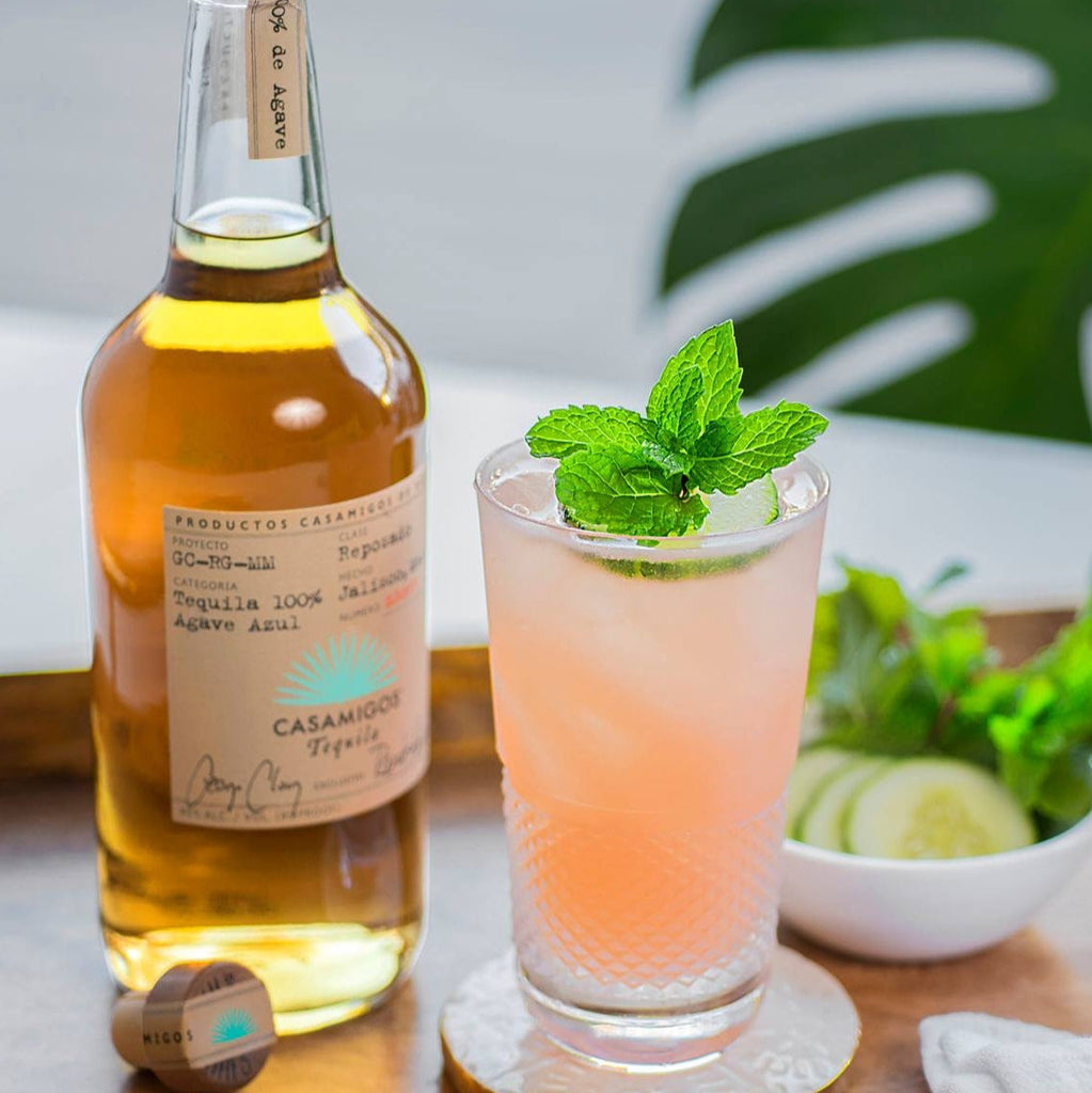 Bottle of Casamigos Reposado tequila with a cocktail garnished with mint leaves on a wooden surface.
