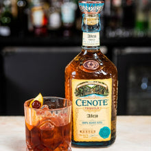 Load image into Gallery viewer, Cenote tequila bottle with a cocktail on a bar counter