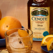 Load image into Gallery viewer, Cenote tequila bottle with a glass of tequila and oranges on a wooden table