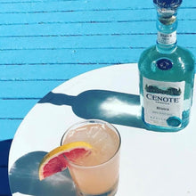 Load image into Gallery viewer, Cenote Blanco bottle with a cocktail and grapefruit wedge on a blue surface