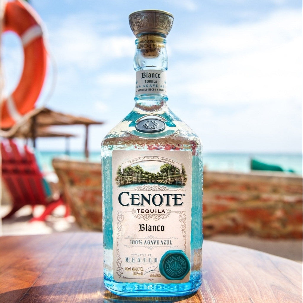 Cenote Blanco Tequila bottle on a wooden surface with a beach background