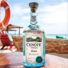 Load image into Gallery viewer, Cenote Blanco Tequila bottle on a wooden surface with a beach background