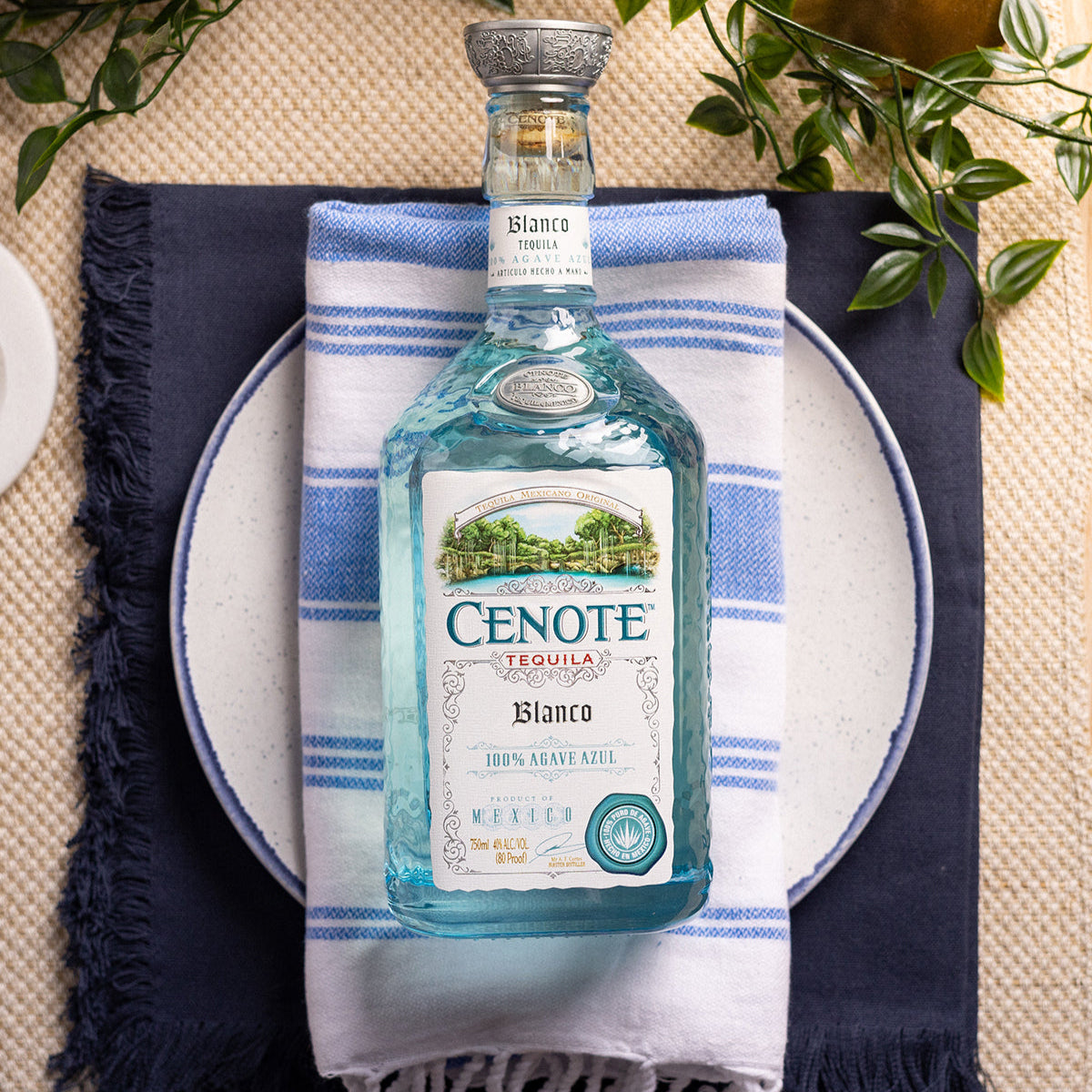 Load image into Gallery viewer, Cenote Blanco Tequila bottle on a blue and white striped towel with greenery in the background