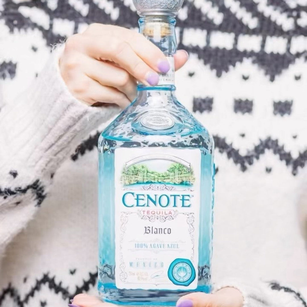 Woman holding a bottle of Cenote Tequila Blanco against a patterned background
