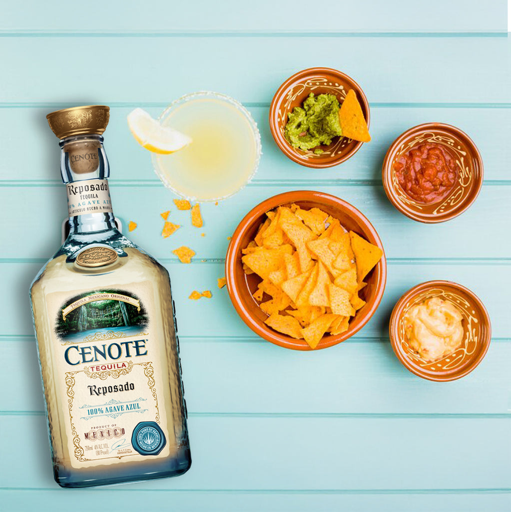 Cenote Reposado tequila bottle with nacho ingredients on a light blue wooden surface