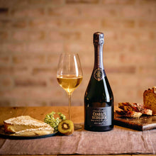Load image into Gallery viewer, Bottle of Charles Heidsieck champagne with a glass and snacks on a wooden table against a brick wall.