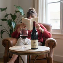 Load image into Gallery viewer, Woman reading a book with a bottle of Charvin Châteauneuf-du-Pape red wine  and a glass on a small table.