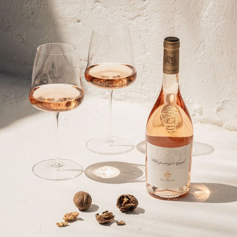 Bottle and two glasses of rose wine on a light surface with a textured wall background