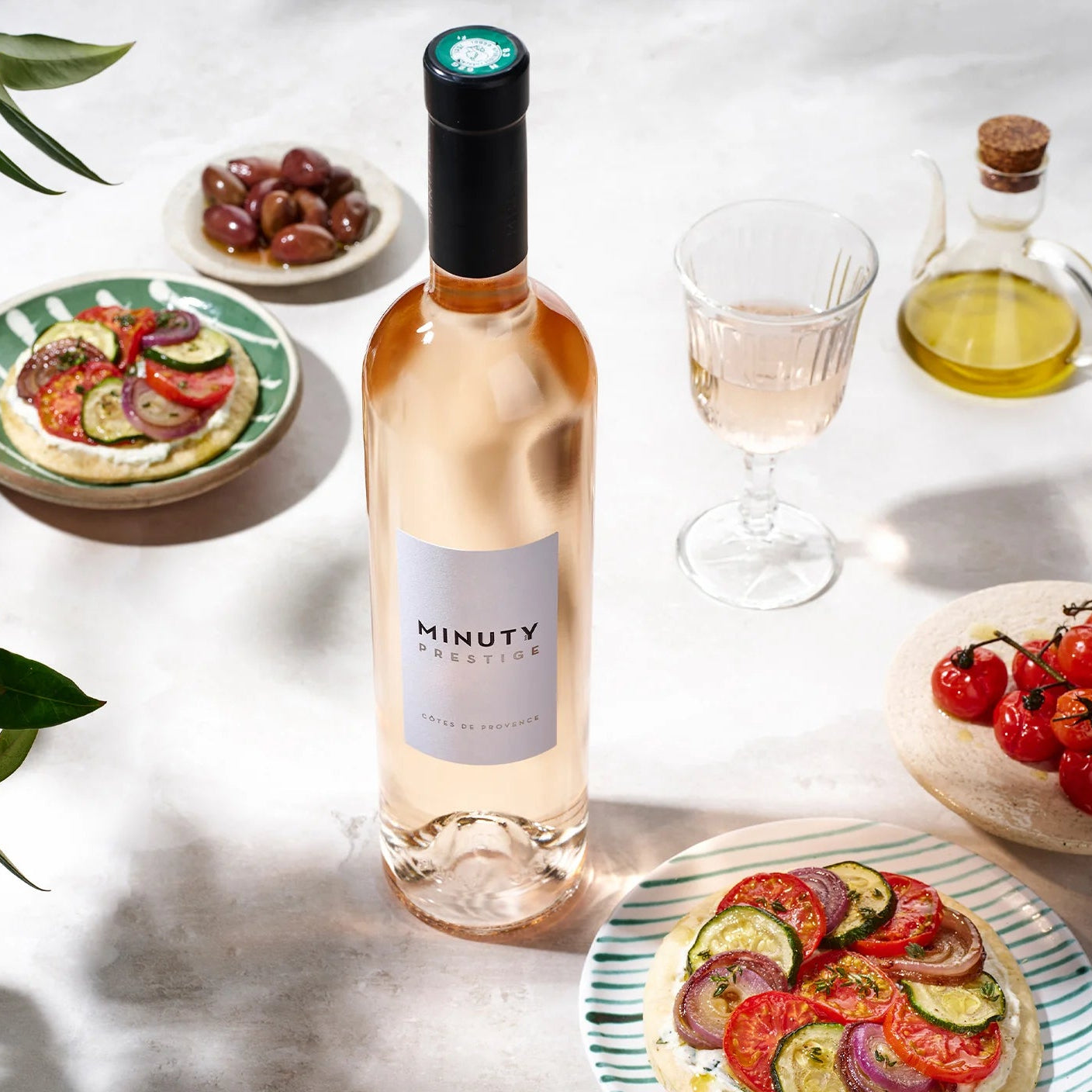 Load image into Gallery viewer, Bottle of Minuty Rosé wine with plates of food on a light surface