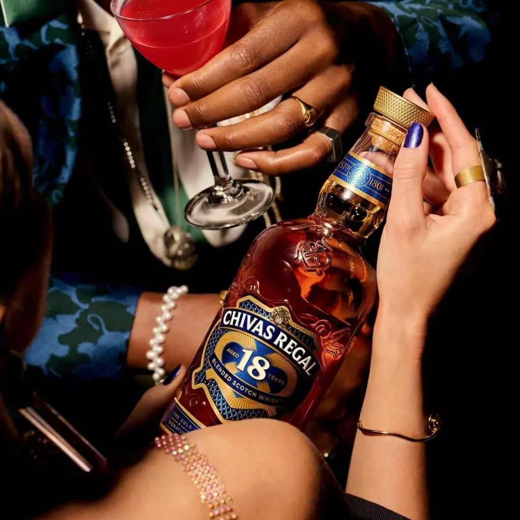 Person holding a bottle of Chivas Regal 18 with a cocktail in the background