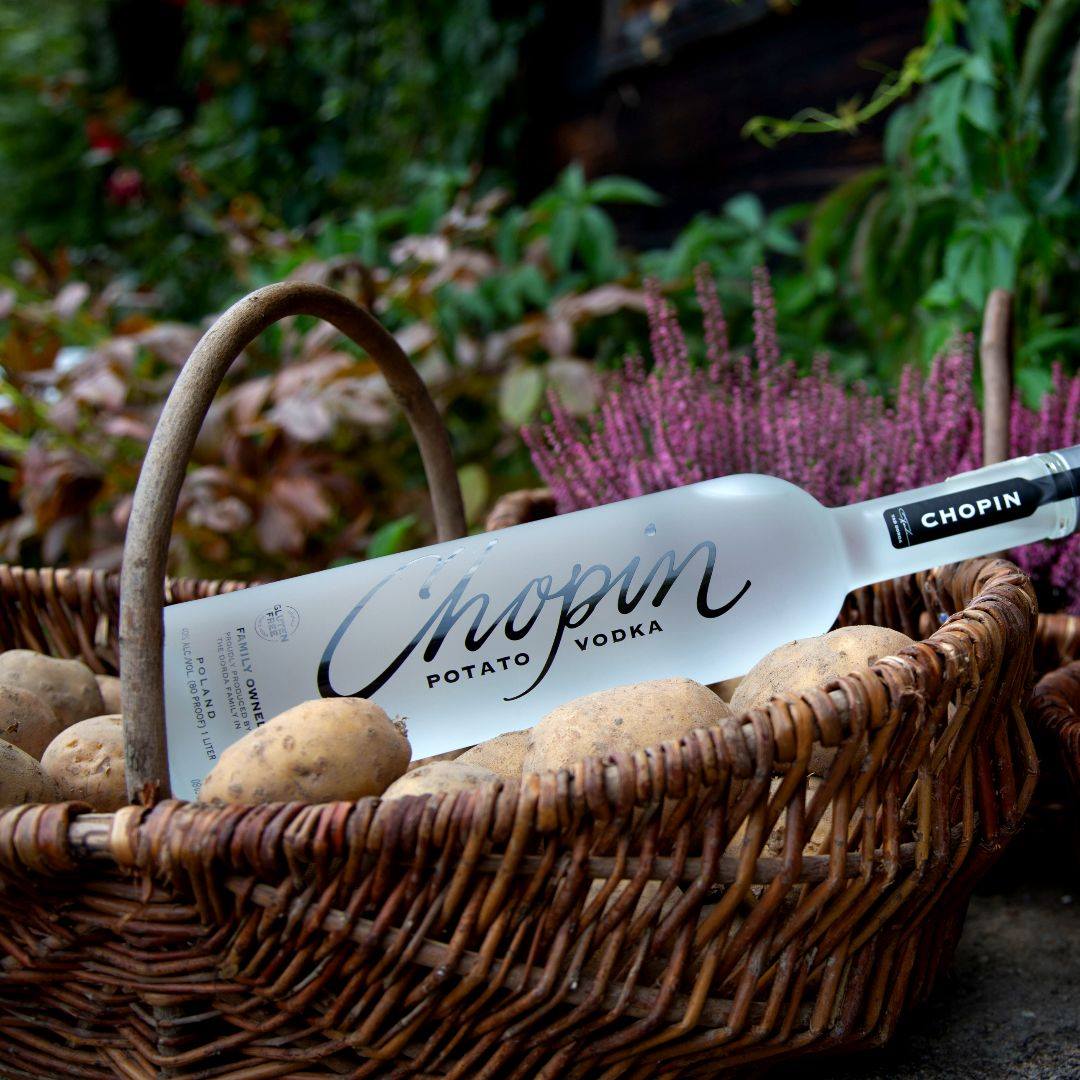 Load image into Gallery viewer, Chopin Potato Vodka bottle inside a basket with potatoes, surrounded by plants.