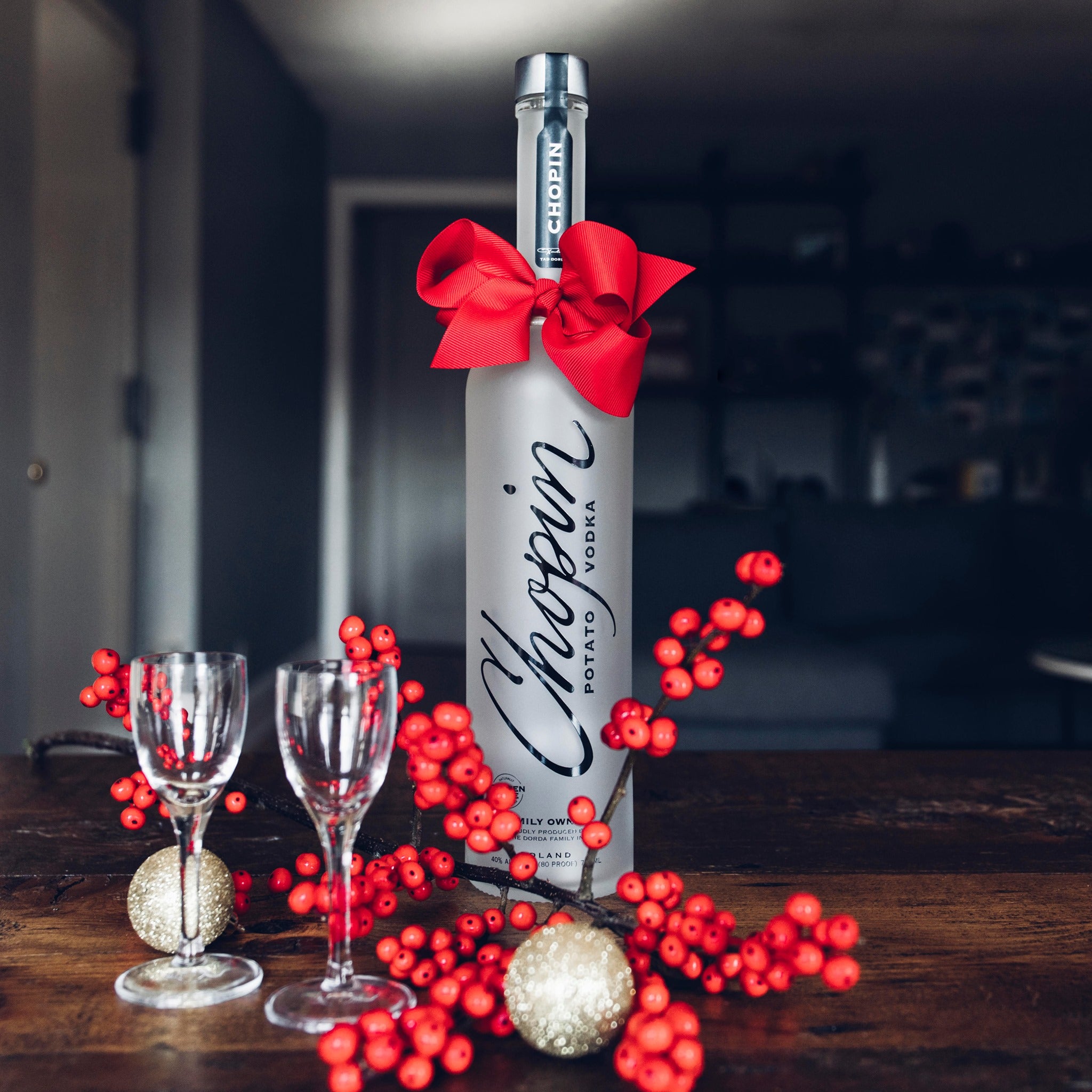 Load image into Gallery viewer, Chopin Potato Vodka bottle with a red bow surrounded by berries and glasses on a wooden surface.
