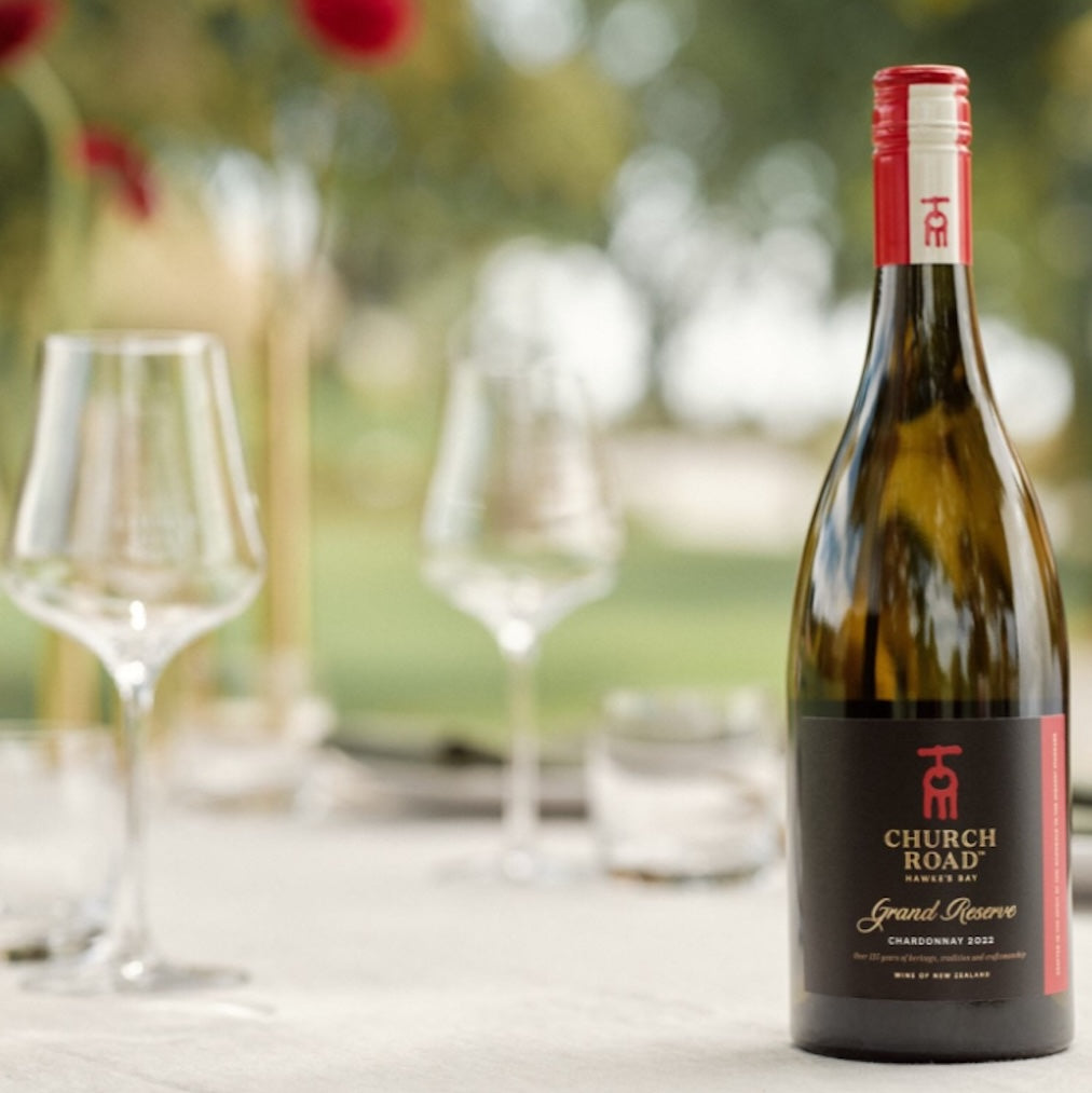 Load image into Gallery viewer, A bottle of Church Road Grand Reserve Chardonnay on a white table with a few glasses in the background