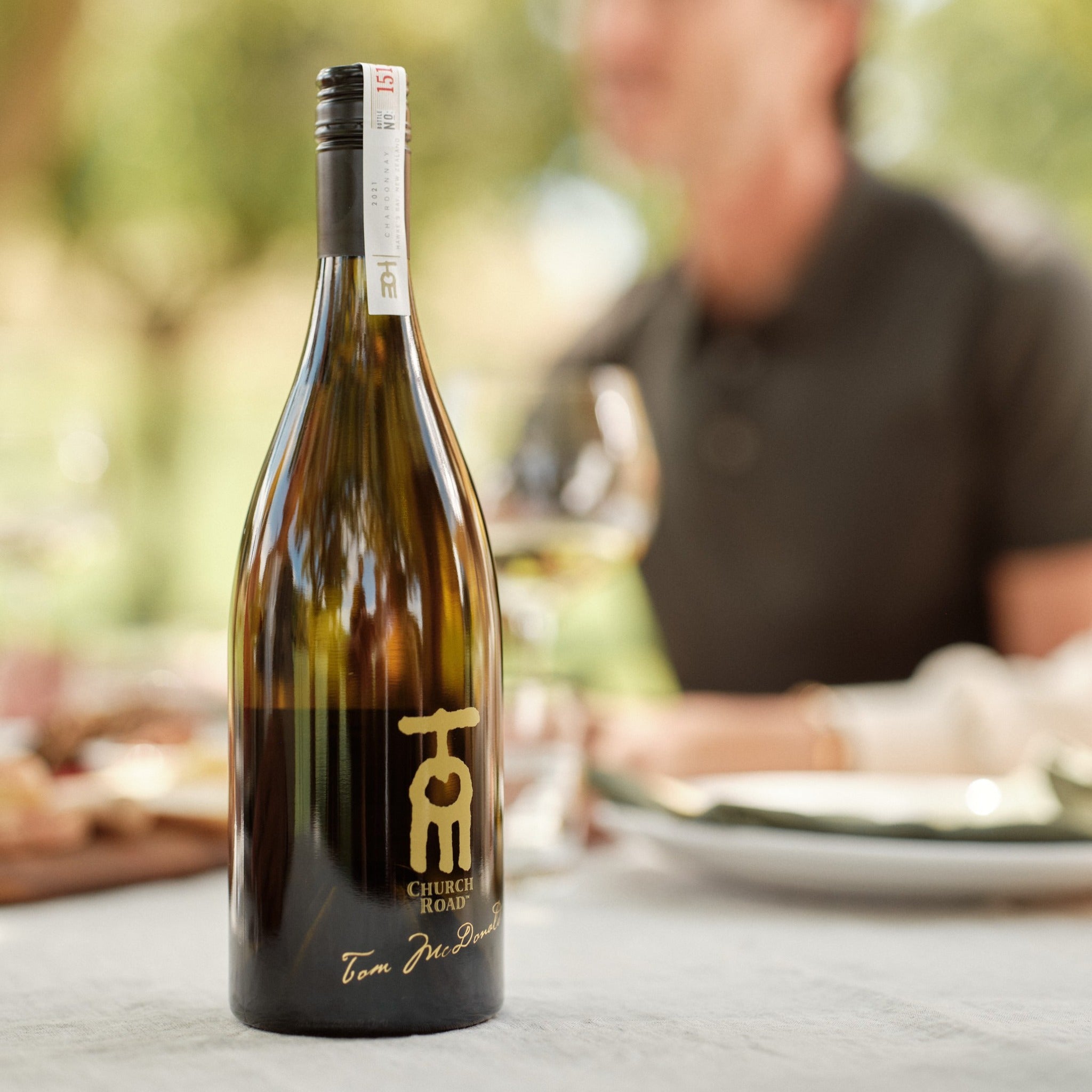Load image into Gallery viewer, Bottle of Church Hill Tom Chardonnay wine on a table with a blurred background of people dining.