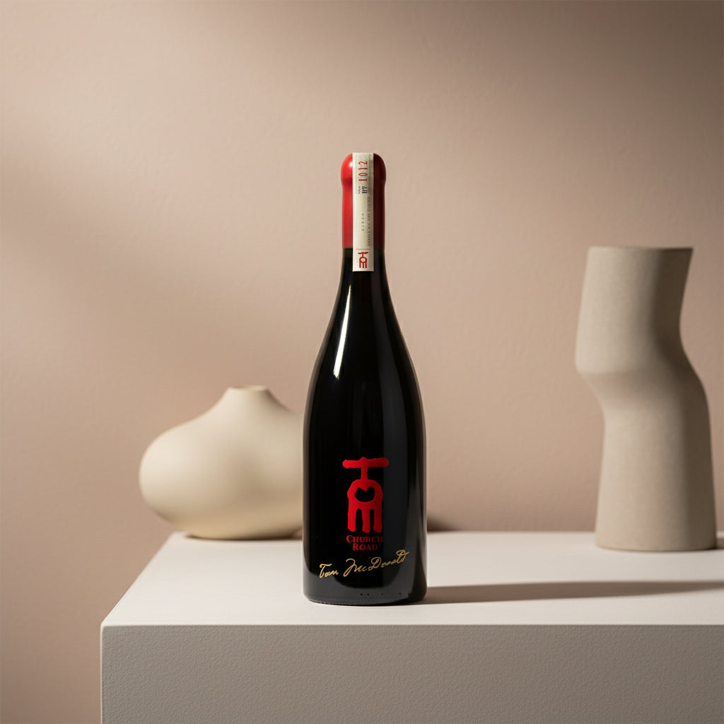 Church Road TOM Syrah-style wine bottle with a red label on a beige surface with decorative vases.