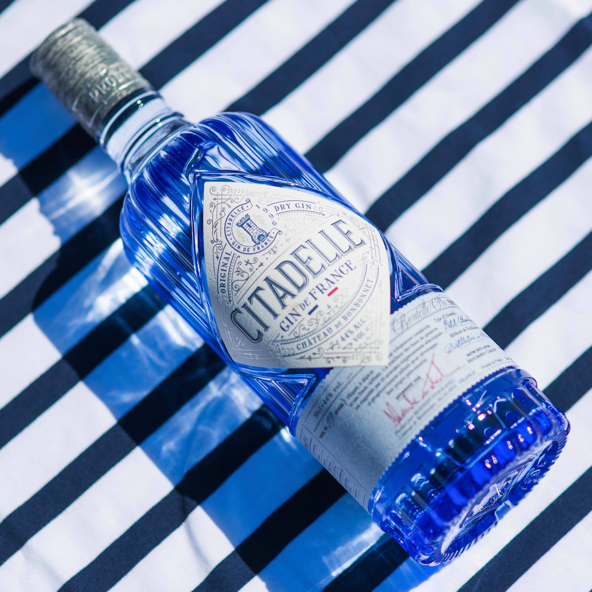 Load image into Gallery viewer, Blue gin bottle with 'Citadelle' label on a striped background