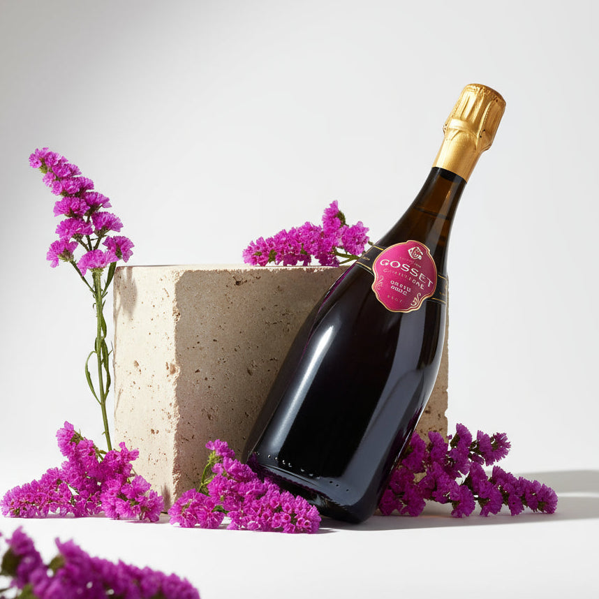 Load image into Gallery viewer, Bottle of Gosset Rosé champagne with a gold cap surrounded by pink flowers on a light background