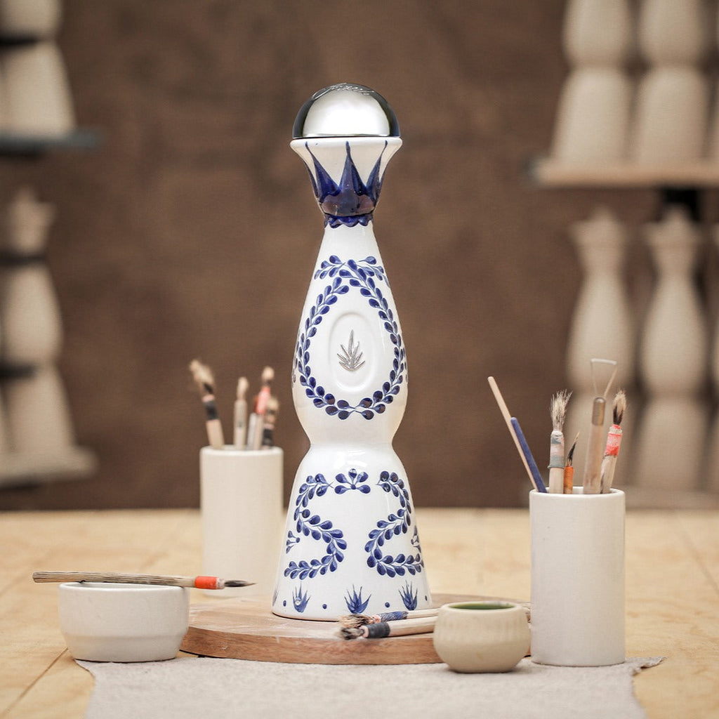 Decorative ceramic Clase Azul Reposado Tequila bottle with artistic design on a wooden surface, surrounded by small containers and tools.