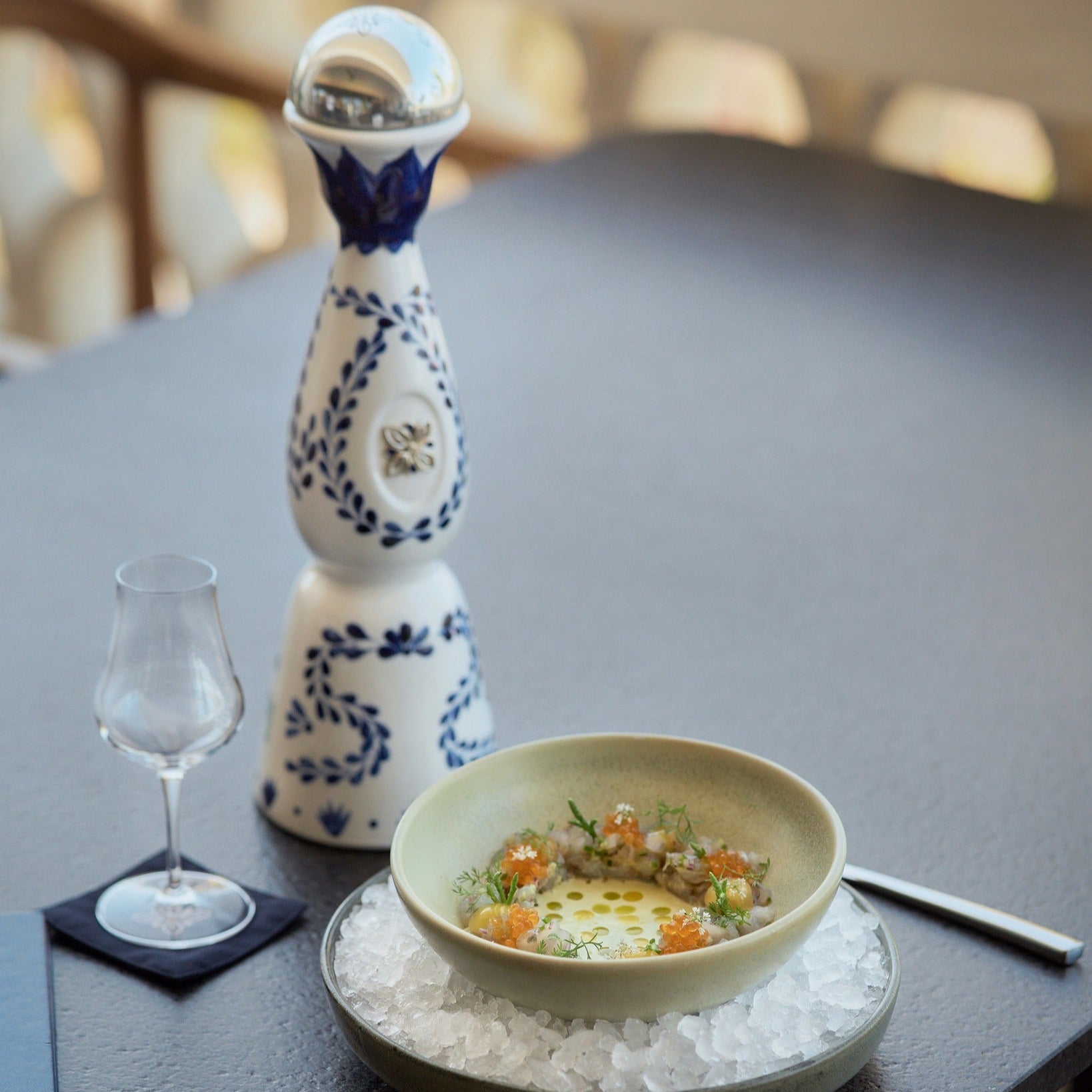 Load image into Gallery viewer, Ceramic bottle of Clase Azul Reposado Tequila with a glass on a table with a dish of food on ice.