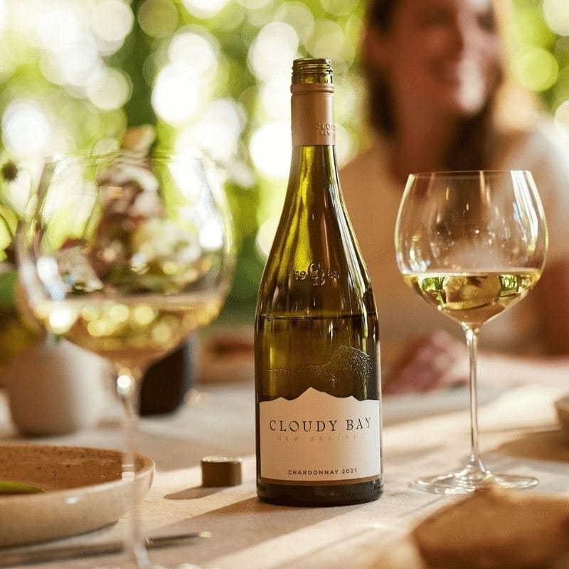 Load image into Gallery viewer, A bottle of white wine and a couple of glasses on a dining table with a woman in the background