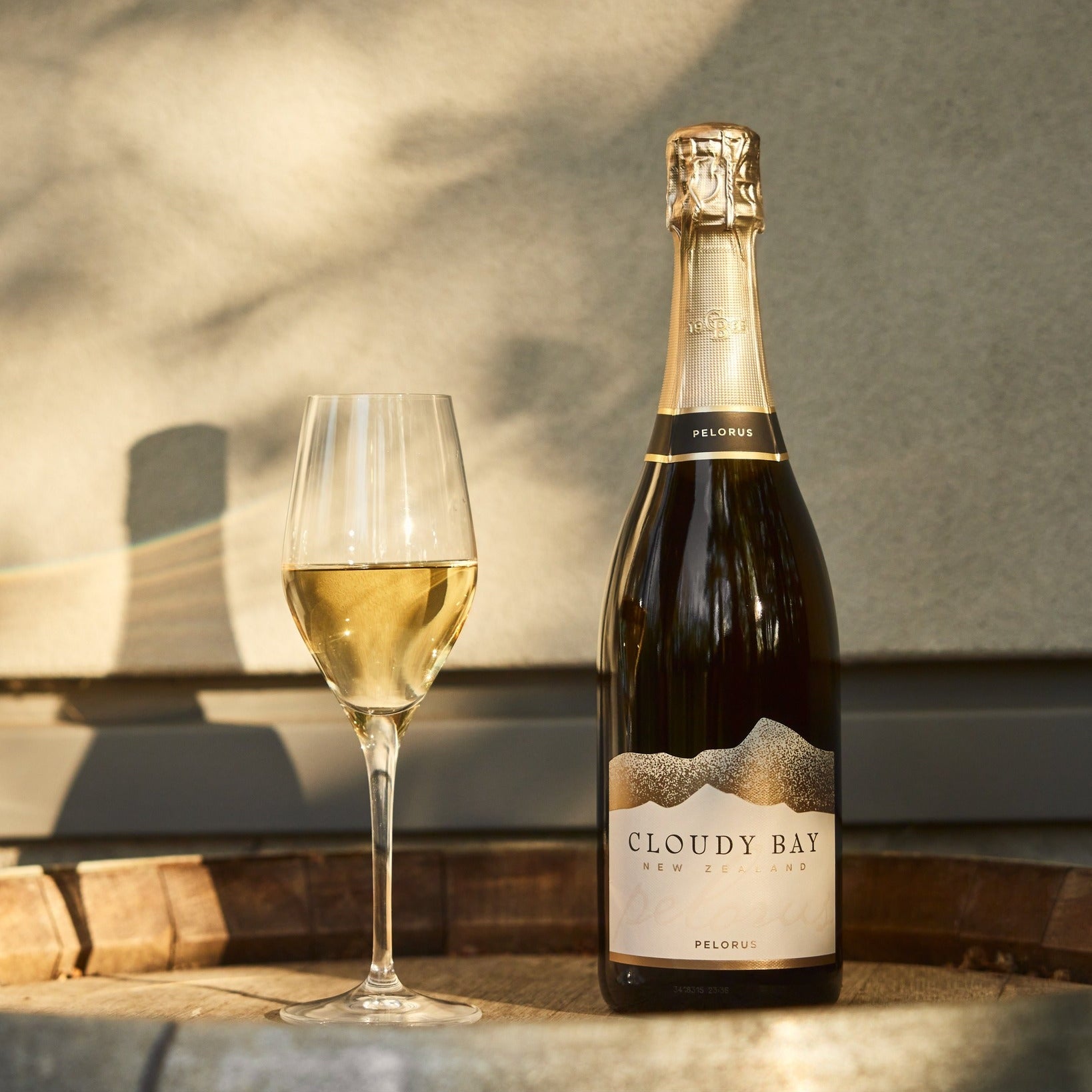 Load image into Gallery viewer, Bottle of Cloudy Bay Pelorus Méthode Traditionnelle sparkling wine with a glass of white wine on a wooden surface.