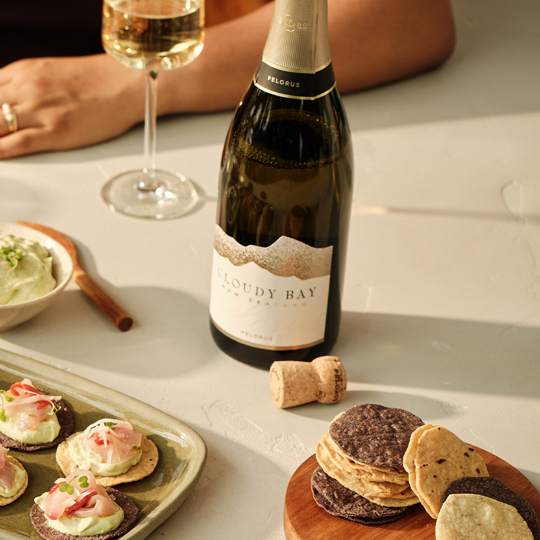 Load image into Gallery viewer, Bottle of Cloudy Bay Pelorus Méthode Traditionnelle sparkling wine with a glass, food, and a cork on a table.