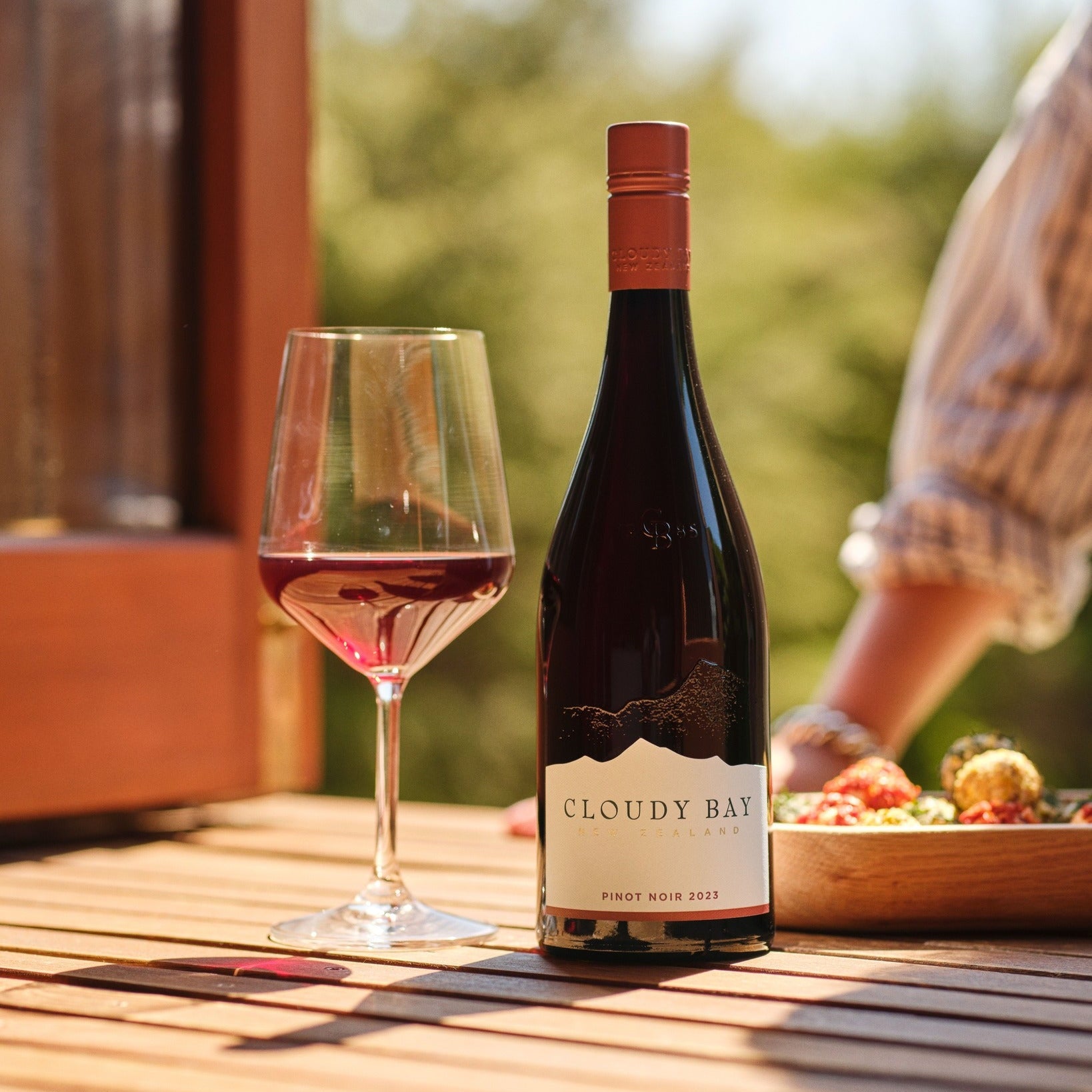 Load image into Gallery viewer, Bottle of Cloudy Bay Pinot Noir with a glass of wine on a wooden table outdoors.