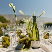 Load image into Gallery viewer, Wine bottle on a table with glasses and flowers outdoors