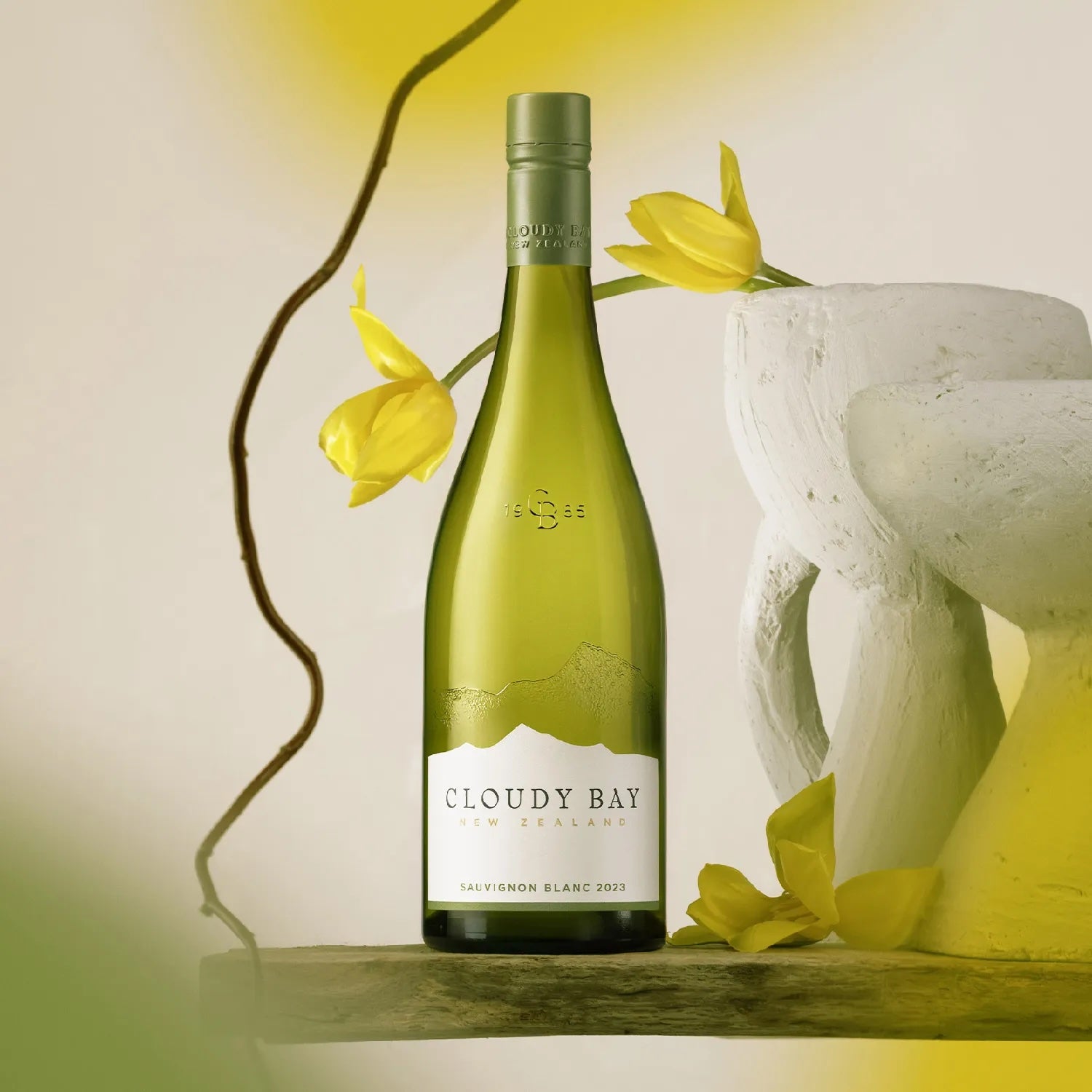 Load image into Gallery viewer, A bottle of Cloudy Bay white wine on a stone table with some yellow tulips behind it